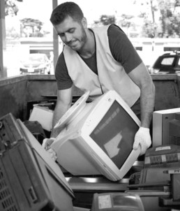 Man lifting old computer from skip bin for recycling
